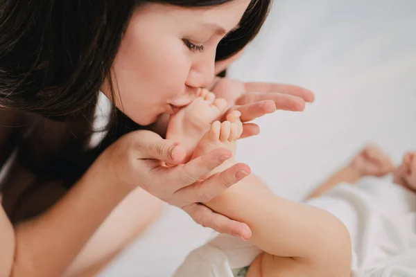 Una madre gentil y cariñosa besa las piernas del bebé. — Foto de Stock