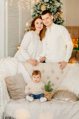 Kanepede küçük bir oğlan, anne ve baba Noel ağacının arkasında kanepenin arkasında.