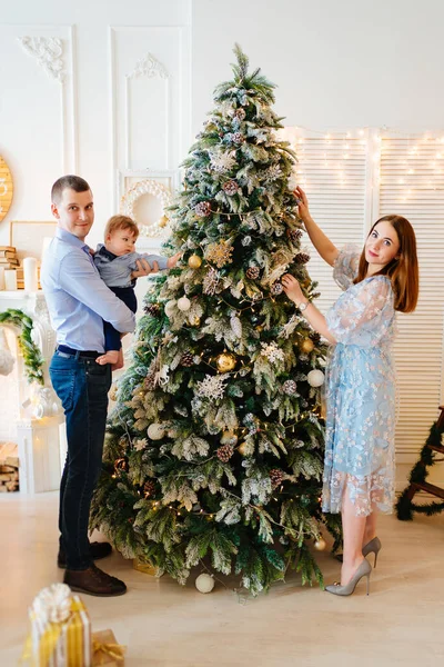 Mutlu ve güzel anne, baba ve küçük oğlu Noel ağacını süslüyor..
