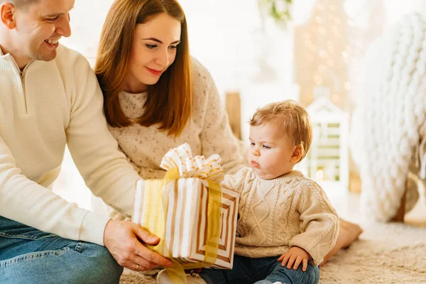 Mama i tata dają prezent w pudełku dla ich młodego syna na podłodze w pokoju. — Zdjęcie stockowe