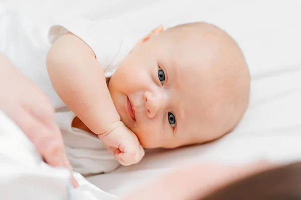 Un lindo bebé con una gota de leche en la esquina de la boca en la cama cerca de la madre. —  Fotos de Stock