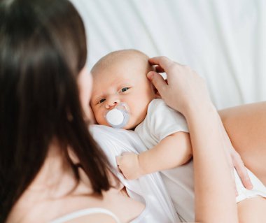 Ağzında emzik, annesinin kollarında bir bebek.