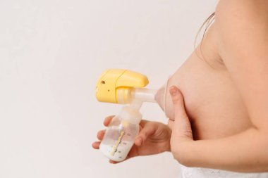 Bir kadın beyaz arka planda meme pompası kullanıyor. Yazı için boşluk. 