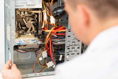 Bir adam atölyedeki bilgisayarı tamir ediyor. Arkadan görünüm