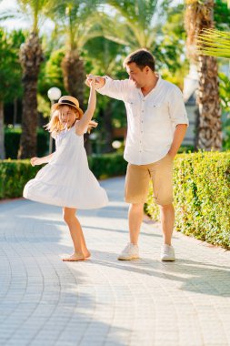 Bir baba ve kızı tropikal bir parkta dans ediyorlar. Babaların ve çocukların tavırları