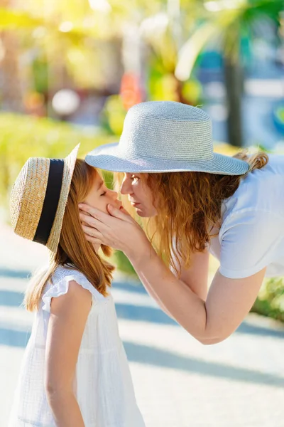 Anne ve kızı otelin tropikal parkında şapka takıyor.