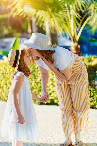 Anne ve kızı otelin tropikal parkında şapka takıyor.