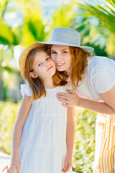 Anne ve kızı otelin tropikal parkında şapka takıyor.