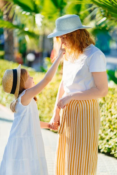 Anne ve kızı otelin tropikal parkında şapka takıyor.