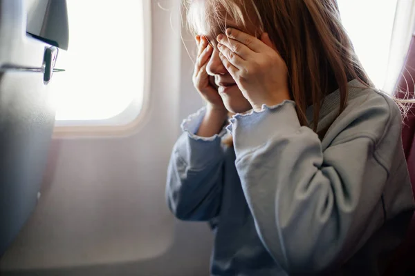 Angst om te vliegen. een kind meisje sluit haar ogen met haar handen in het vliegtuig stoel — Stockfoto