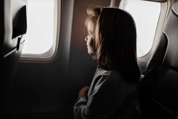 A little girl sits in an airplane seat by the window. — Stockfoto