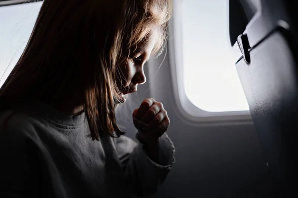 En liten flicka sitter och hostar i ett flygplanssäte vid fönstret. — Stockfoto