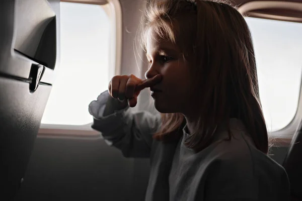 A little girl clamps nose because of unpleasant smell in airplane seat by window — Stockfoto
