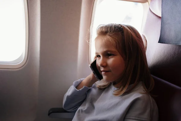 A little girl is talking on the phone in an airplane seat — 图库照片