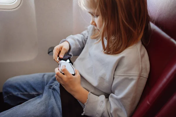 A little girl fastens her seat belt in a seat on board the plane. — 图库照片