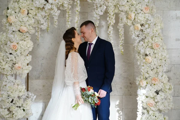 Gyönyörű és boldog menyasszony és a vőlegény egy boltíves virág az esküvői ceremónián — Stock Fotó