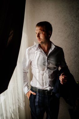 Beyaz gömlekli bir adam pencerede duran bir ceket tutuyor.