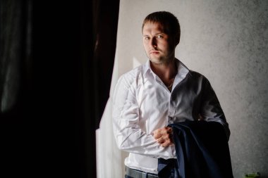 Beyaz gömlekli bir adam pencerede duran bir ceket tutuyor.