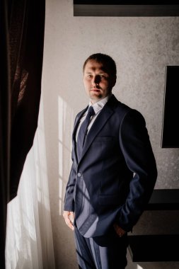 Beyaz gömlekli, ceketli ve kravatlı bir adam pencerede duruyordu.