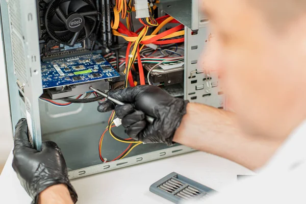 Bir adam atölyedeki bilgisayarı tamir ediyor. Arkadan görünüm