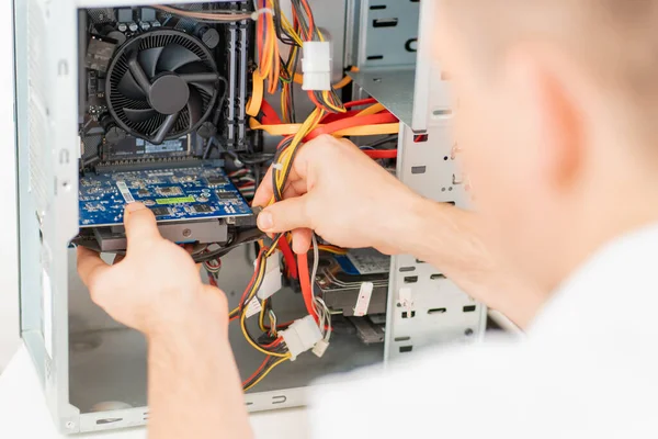 Bir adam atölyedeki bilgisayarı tamir ediyor. Arkadan görünüm