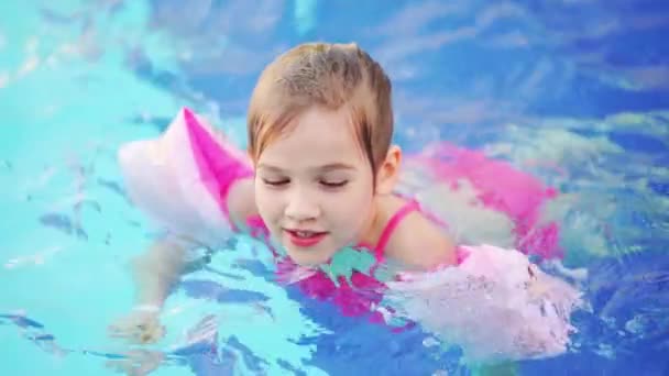 Uma menina engraçada nada e joga em braçadeiras infláveis em uma piscina — Vídeo de Stock