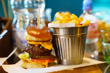 Bir kova patates kızartması ve pirzola, domates, peynir ve sostan yapılmış mini burger..