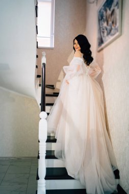 Gelin, uzun beyaz gelinlik içinde, trenle merdivenlerden çıkıyor.. 