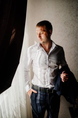 Beyaz gömlekli bir adam pencerede duran bir ceket tutuyor.