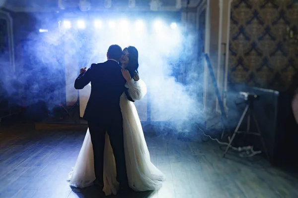 The bride and groom in wedding dresses dance in a dark hall in heavy smoke. — Stockfoto