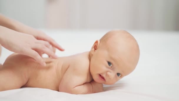 A baba a hasán fekszik egy fehér lepedőn. és anyák kéz masszázs a hátsó. — Stock videók