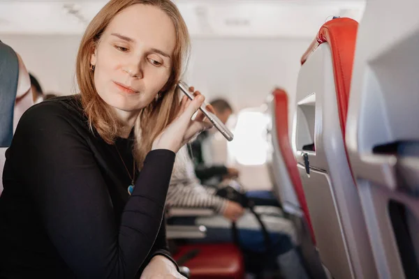 Kvinna lyssnar på ett röstmeddelande på telefonen i en plats ombord på planet. — Stockfoto