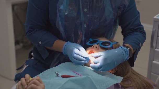 Стоматолог осматривает зубы маленькой девочки на приеме. — стоковое видео