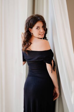 Pencerenin yanında siyah elbiseli çekici hamile bir kadın.