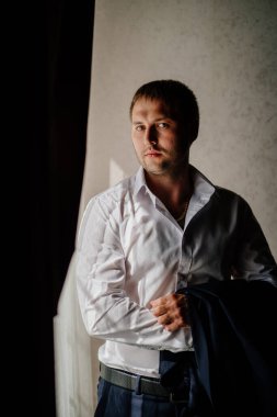 Beyaz gömlekli bir adam pencerede duran bir ceket tutuyor.