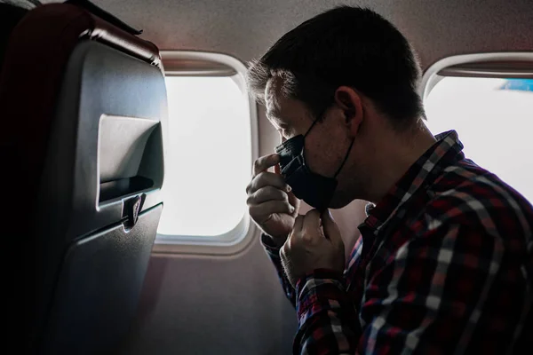男は黒い保護マスクを修正し、飛行機の窓からシャツを再生. — ストック写真