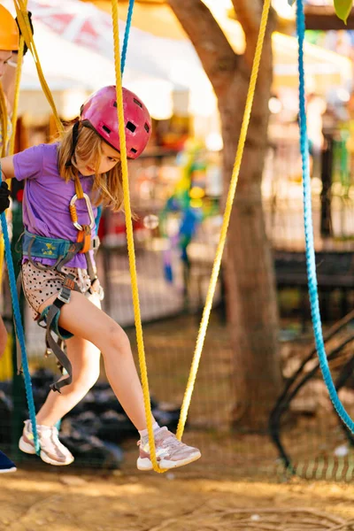 Valiente chica en casco, camiseta y pantalones cortos sube en el parque de cuerdas. lucha contra el miedo. — Foto de Stock