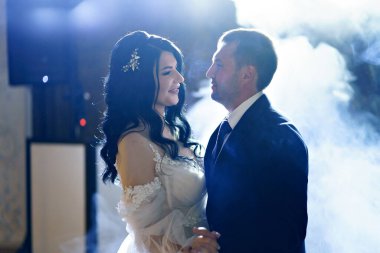 Gelinlik giymiş gelin ve damat ağır dumanla karanlık bir salonda dans ediyor..