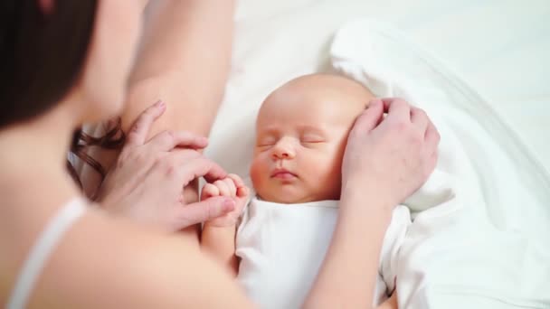 Mamá se sienta en la cama y mira al bebé dormido. la felicidad de la maternidad. — Vídeo de stock