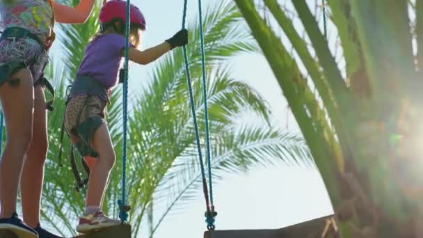 Frightened but brave girls in helmet, T-shirt and shorts climbs in rope park — Αρχείο Βίντεο