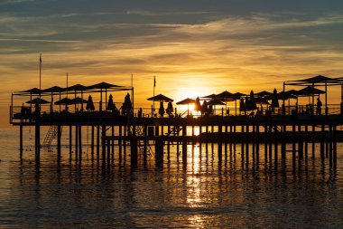 Şemsiyeli ve güneşli iskelede. Siluetler. Denizde güzel gün batımı. 