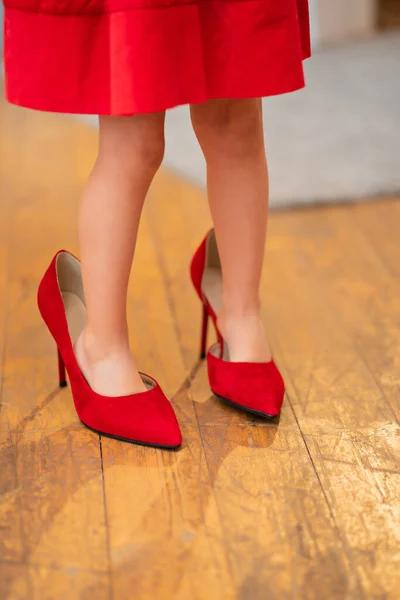 Los pies de una niña en sus zapatos de tacón rojo de las madres. — Foto de Stock