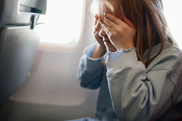 Fear of flying. a kid girl closes her eyes with her hands in the airplane seat — Stockfoto
