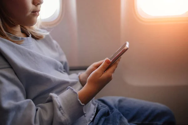 Händer en liten flicka spelar spel på smartphone i ett flygplan säte — Stockfoto