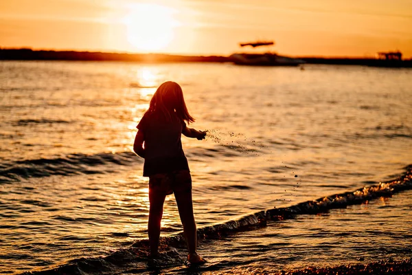 На закате. Девочка ходит по берегу моря, собирает камни и бросает их в воду. — стоковое фото