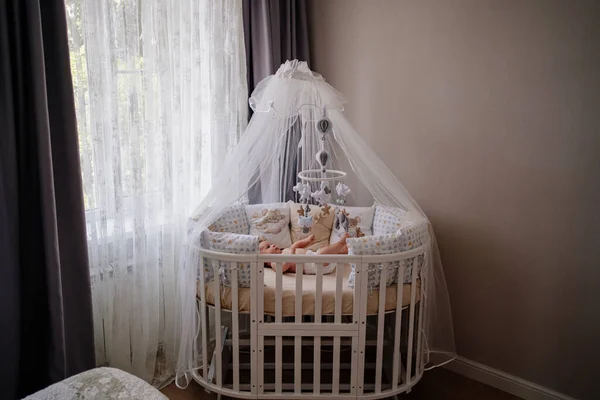 A baby lies in a white crib with a canopy. furniture for the childrens room. — Foto de Stock