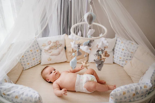 Vista desde arriba. un bebé se encuentra en una cuna blanca con móvil con juguetes. — Foto de Stock