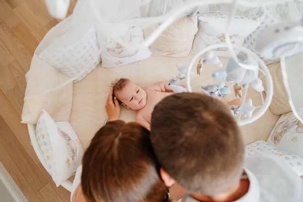 Vista desde arriba. padres a un bebé se encuentra en una cuna blanca con móvil con juguetes. — Foto de Stock