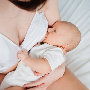 breastfeeding. mother in silk nightshirt feeds baby with breast milk. close up.