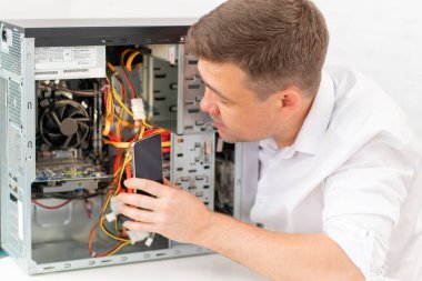 Beyazlı bir adam atölyedeki bozuk bir bilgisayara el feneri tutuyor.